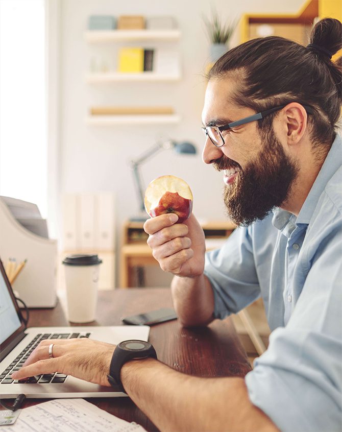 Employee working on a laptop and enjoying eating apple and having a cup of coffee